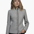Front view of a woman wearing a light gray tailored jacket with a stand-up collar trimmed in dark green. A vertical row of small metallic buttons runs down the front, and the fitted silhouette is styled with dark jeans. The background is plain light gray.