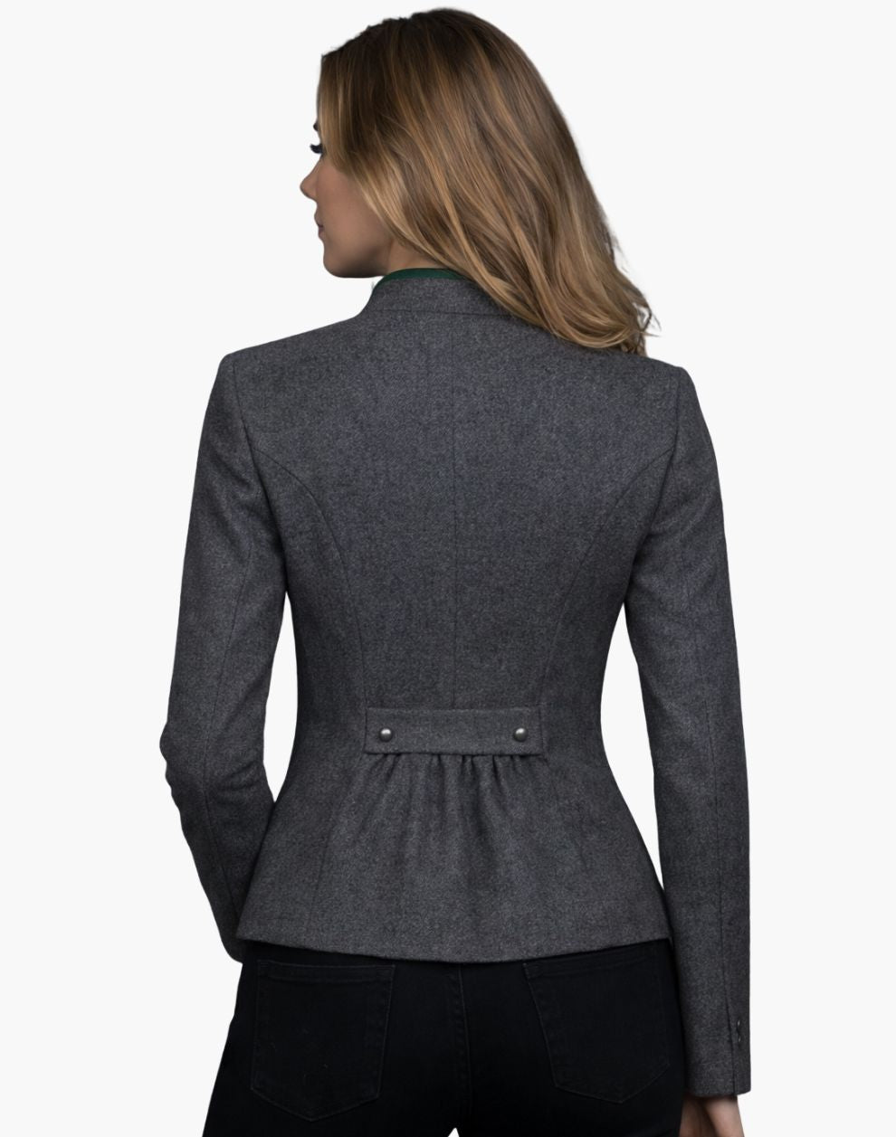 Back view of a woman wearing a fitted charcoal gray wool jacket with structured seam lines and a peplum-style hem. A decorative back tab with two buttons accents the waist, with soft gathers below it. She pairs the jacket with dark jeans, and her shoulder-length blonde hair falls over a green-trimmed collar. The background is plain light gray in a studio setting.