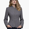 Woman wearing a light grey Trachten-style jacket with decorative buttons, high collar, and a fitted tailored design, paired with dark jeans, against a white background.