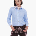 Woman wearing embroidered brown leather lederhosen shorts with a blue gingham shirt and a light pink neck scarf, styled in traditional Bavarian Oktoberfest fashion.