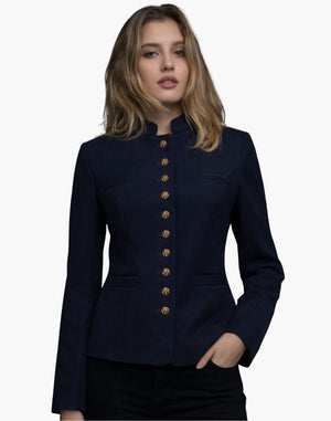 Front view of a woman wearing a deep navy tailored jacket with a stand-up collar and a vertical row of gold-tone buttons down the front. The fitted silhouette features subtle welt pockets and structured seams, styled with dark jeans. The background is plain light gray.