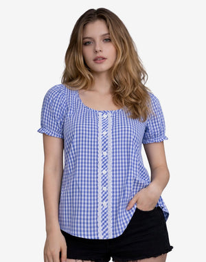 Front view of a woman wearing a blue and white gingham dirndl blouse with short puff sleeves, lace trim and button detail, paired with black denim shorts.